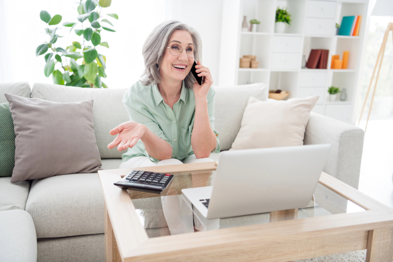 Photo of cheerful person sit on couch speak phone arm palm explain tell have good mood toothy smile indoors.